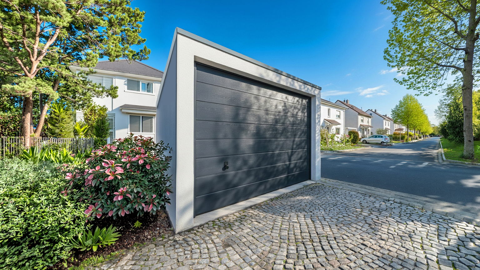 Moderne Betonfertiggarage mit dunklem Sektionaltor an ruhiger Wohnstraße Freistehende Betonfertiggarage mit großem dunklem Sektionaltor und Flachdach an einer gepflasterten Einfahrt, umgeben von Gartenpflanzen und Bäumen in einer ruhigen Wohnsiedlung mit Einfamilienhäusern, ZAPF Garagen