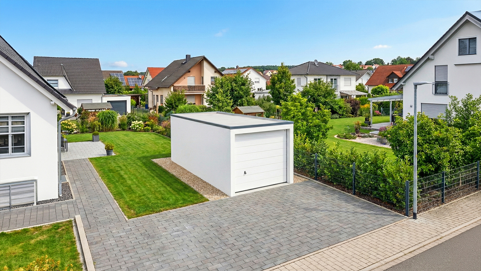 Detached precast concrete garage with white sectional door in residential area Detached precast concrete garage with white sectional garage door and flat roof on a paved driveway, surrounded by a landscaped garden and single-family homes in a residential neighborhood by ZAPF