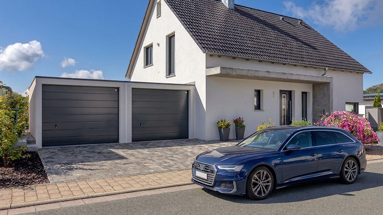 Eine Doppelgarage neben einem Einfamilienhaus, davor ein Auto, das die Einfahrt der Straße blockiert.