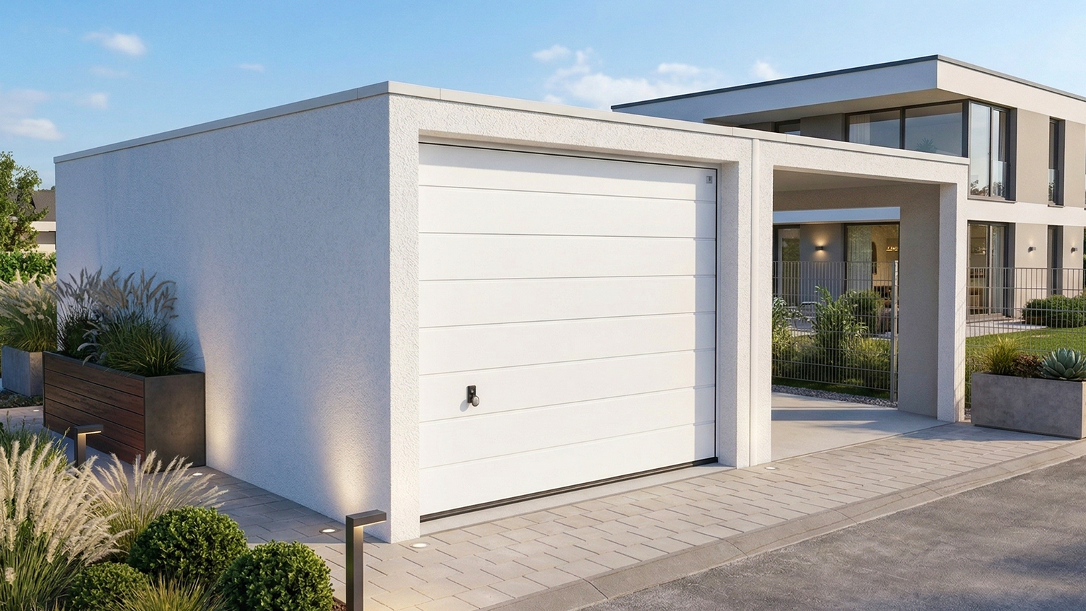Moderne Betonfertiggarage mit Sektionaltor neben Einfamilienhaus Helle Betonfertiggarage mit glattem Putz und weißem Sektionaltor vor einem modernen Wohnhaus, gepflasterte Einfahrt, bepflanzte Beete und klare Architektur, ZAPF Garagen