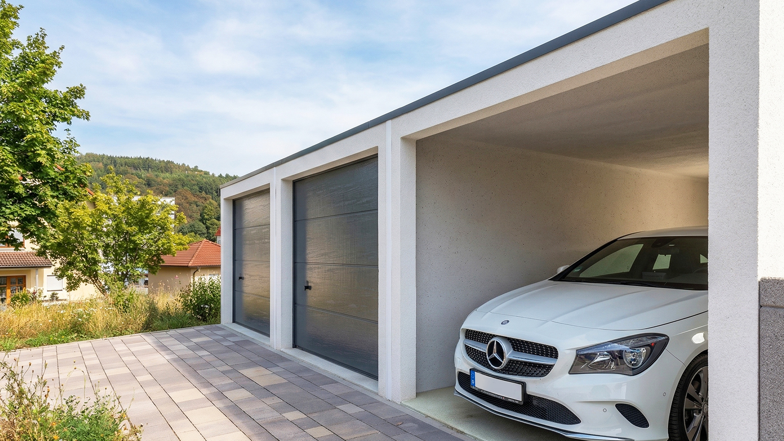 Betonfertiggarage mit Doppel-Sektionaltor und offenem Stellplatz Moderne Betonfertiggarage mit zwei dunklen Sektionaltoren und seitlich offenem Stellplatz mit geparktem Fahrzeug, gepflasterte Einfahrt, Wohnumgebung mit Bäumen und Einfamilienhäusern, ZAPF Garagen