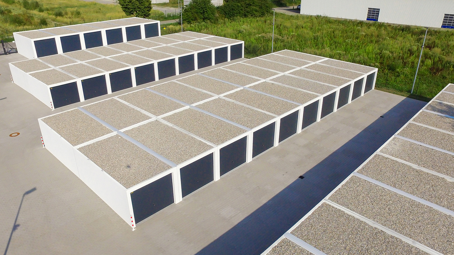 Reihengaragenanlage aus Betonfertiggaragen mit Flachdach und dunklen Sektionaltoren Luftaufnahme einer großflächigen Anlage mit weißen Betonfertiggaragen in Reihen, Flachdächer mit Kiesauflage und gleichmäßig angeordnete dunkle Garagentore auf befestigter Fläche von ZAPF