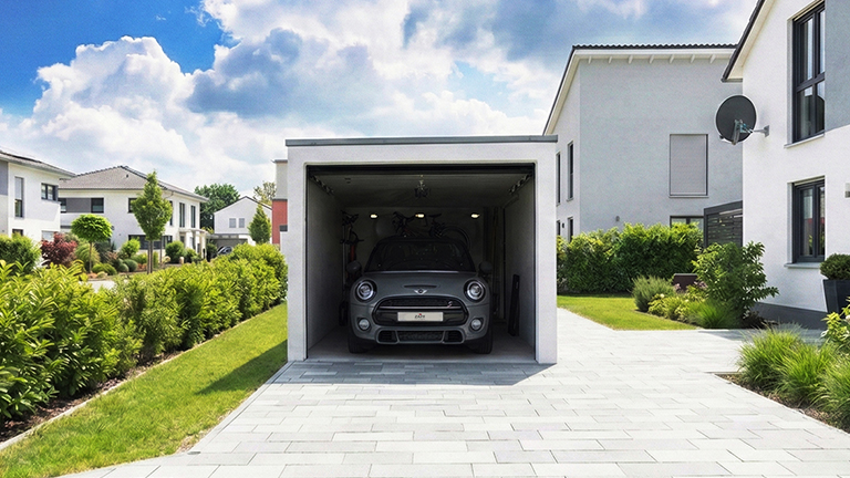 Weiße Fertiggarage mit geöffnetem Garagentor, geparktem Auto und Fahrrädern auf dem Dachträger vor einem modernen Einfamilienhaus mit gepflasterter Einfahrt und grüner Gartenanlage von ZAPF