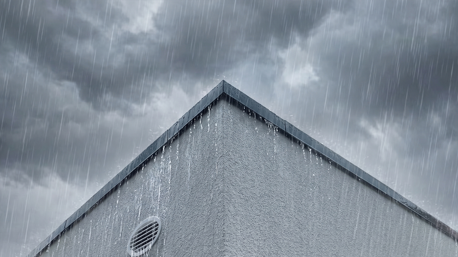 Betonfertiggarage bei starkem Regen Nahaufnahme einer grauen Betonfertiggarage mit dunkler Dachkante, Lüftungsgitter und ablaufendem Regenwasser vor bewölktem Himmel, vom Hersteller ZAPF