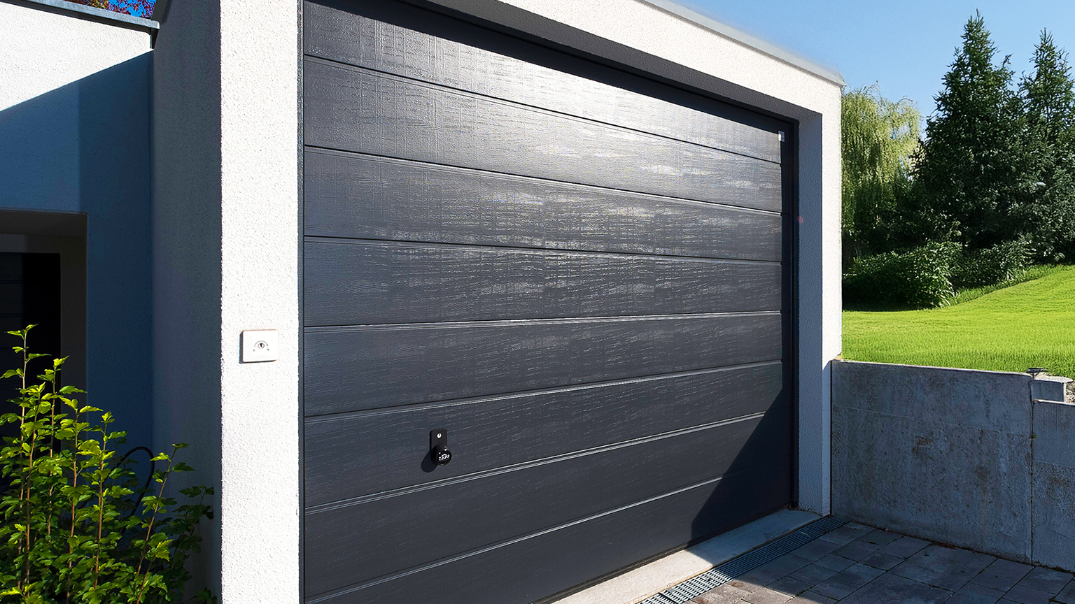 Betonfertiggarage mit dunklem Sektionaltor Moderne Betonfertiggarage mit hellem Baukörper, dunklem Sektionaltor in Holzoptik, gepflasterter Zufahrt und Grünfläche im Hintergrund von ZAPF